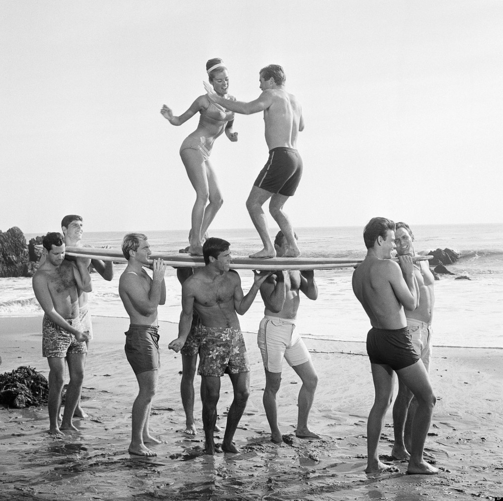 File-This 1965 file photo of youthful actors in a Hollywood movie amuse themselves between shooting of scenes at California's Malibu Beach by staging an airborne twist exhibition on top of a surf board. Annette Funicello helped create a world as fanciful as Walt Disney's Magic Kingdom when she traded in her Mousketeer ears for a modest one-piece bathing suit . It was a land of perfect waves and sparkling sand, in a place where there was a beach party every night and summer never ended. (AP Photo, File)